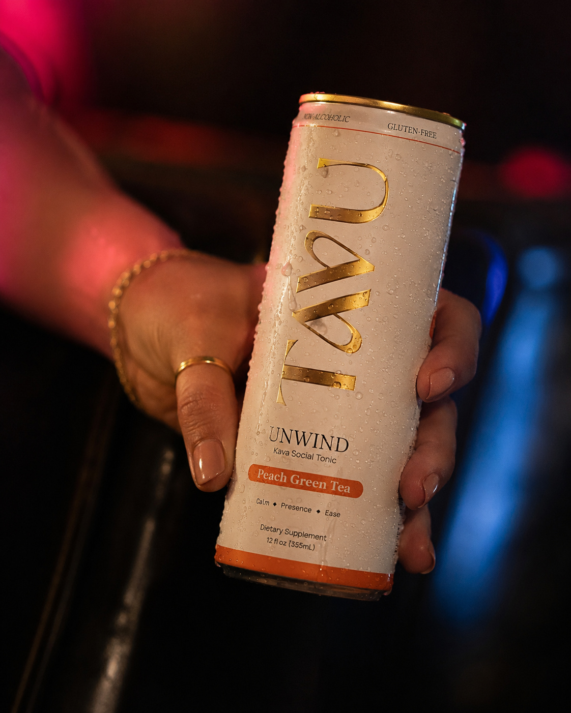 A hand holding a TAVU Peach Green Tea kava social tonic at a dimly lit bar