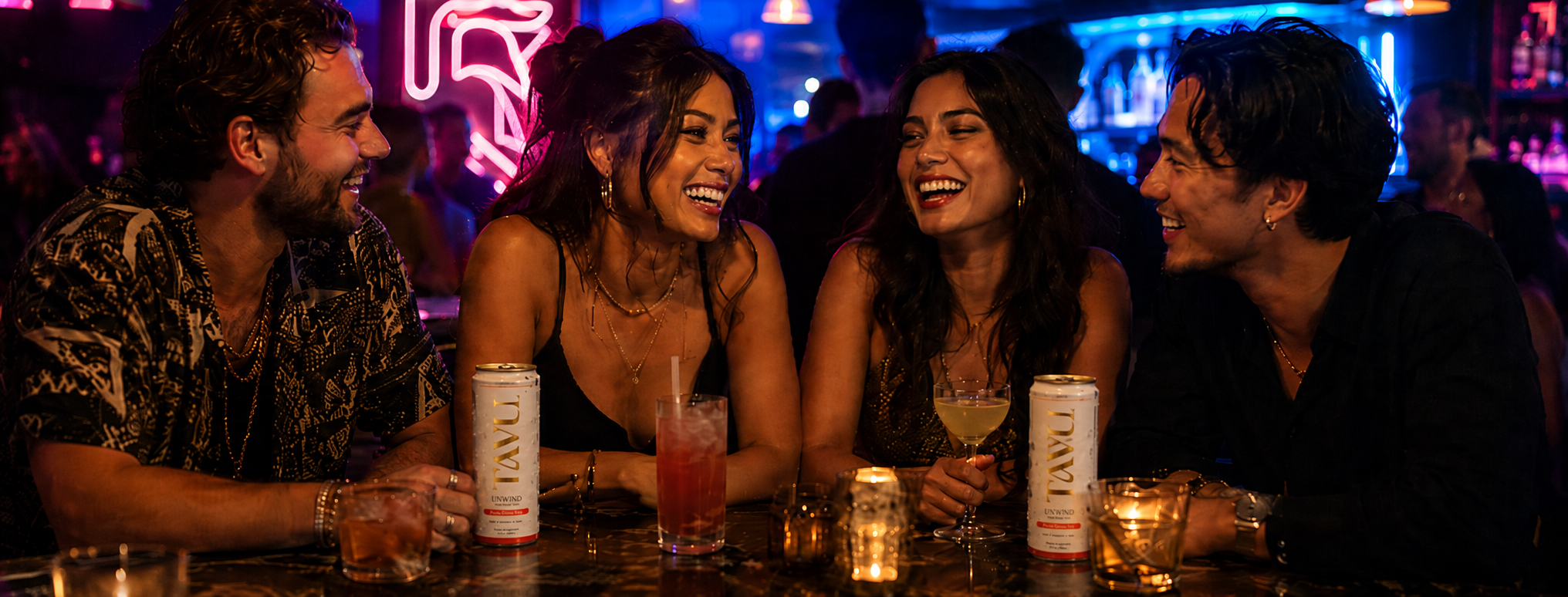 Four friends laughing together over TAVU cans at a bar at night